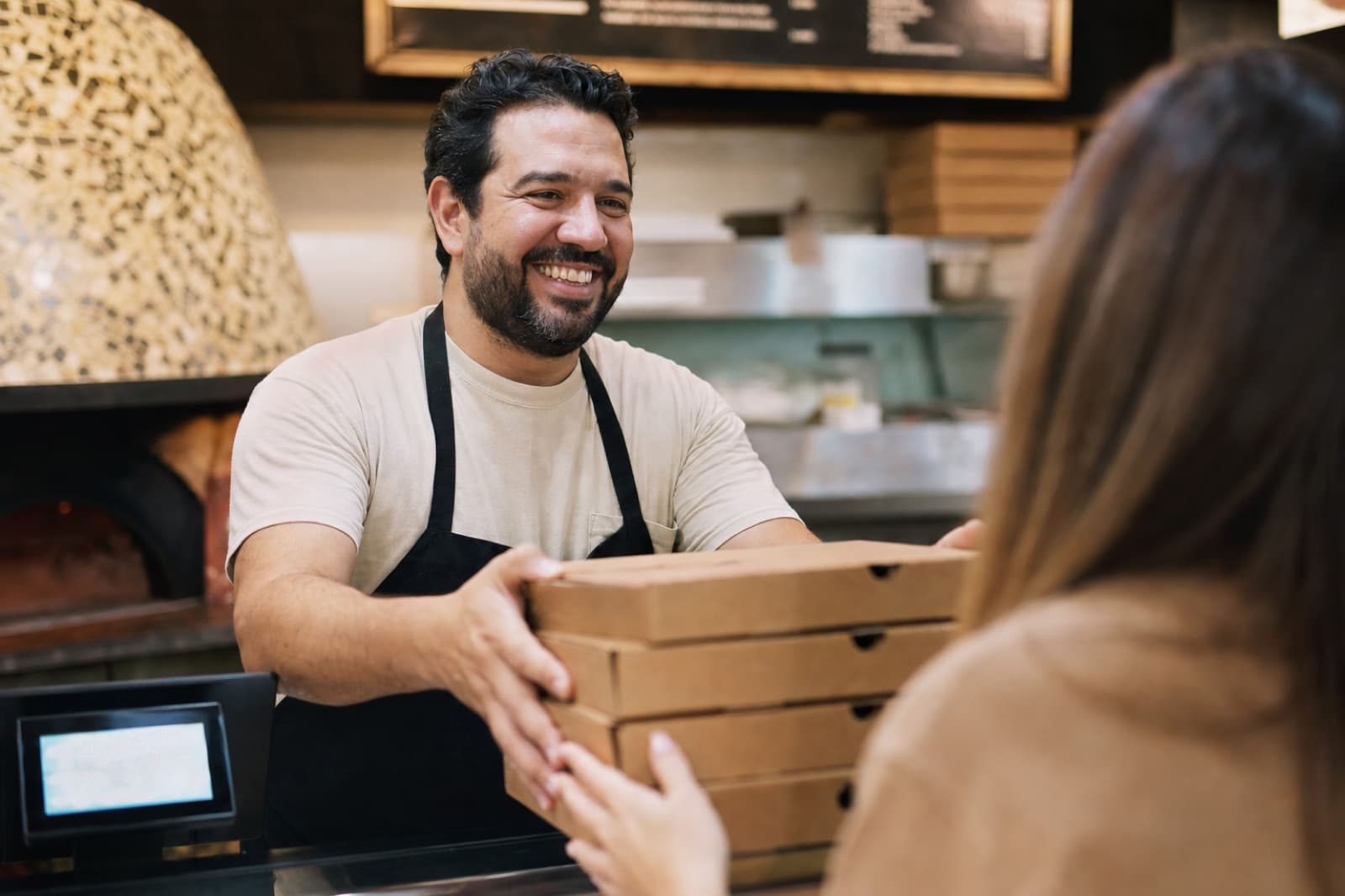 Pizzeria owner handing takeout boxes to a regular customer across the counter