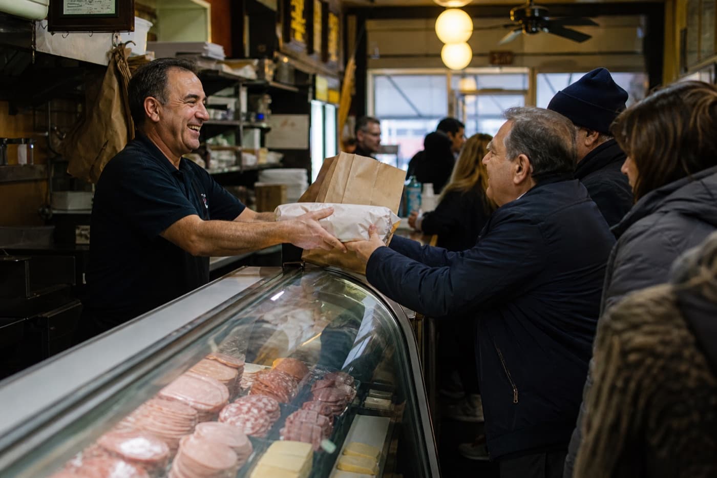 Deli owner handing a wrapped sub across the counter